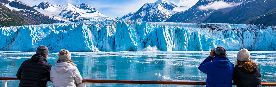 Cruise passengers watch a massive blue glacier calving into icy waters during an Alaska glacier-viewing cruise.