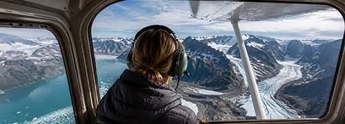 An Alaska flightseeing passenger views glaciers, rugged mountain ranges, and turquoise coastal waters from a small aircraft.