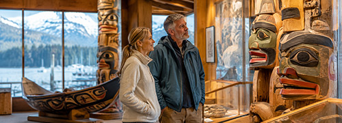 Alaska visitors explore Native artwork, carved totem poles, and regional history exhibits at a waterfront cultural museum.